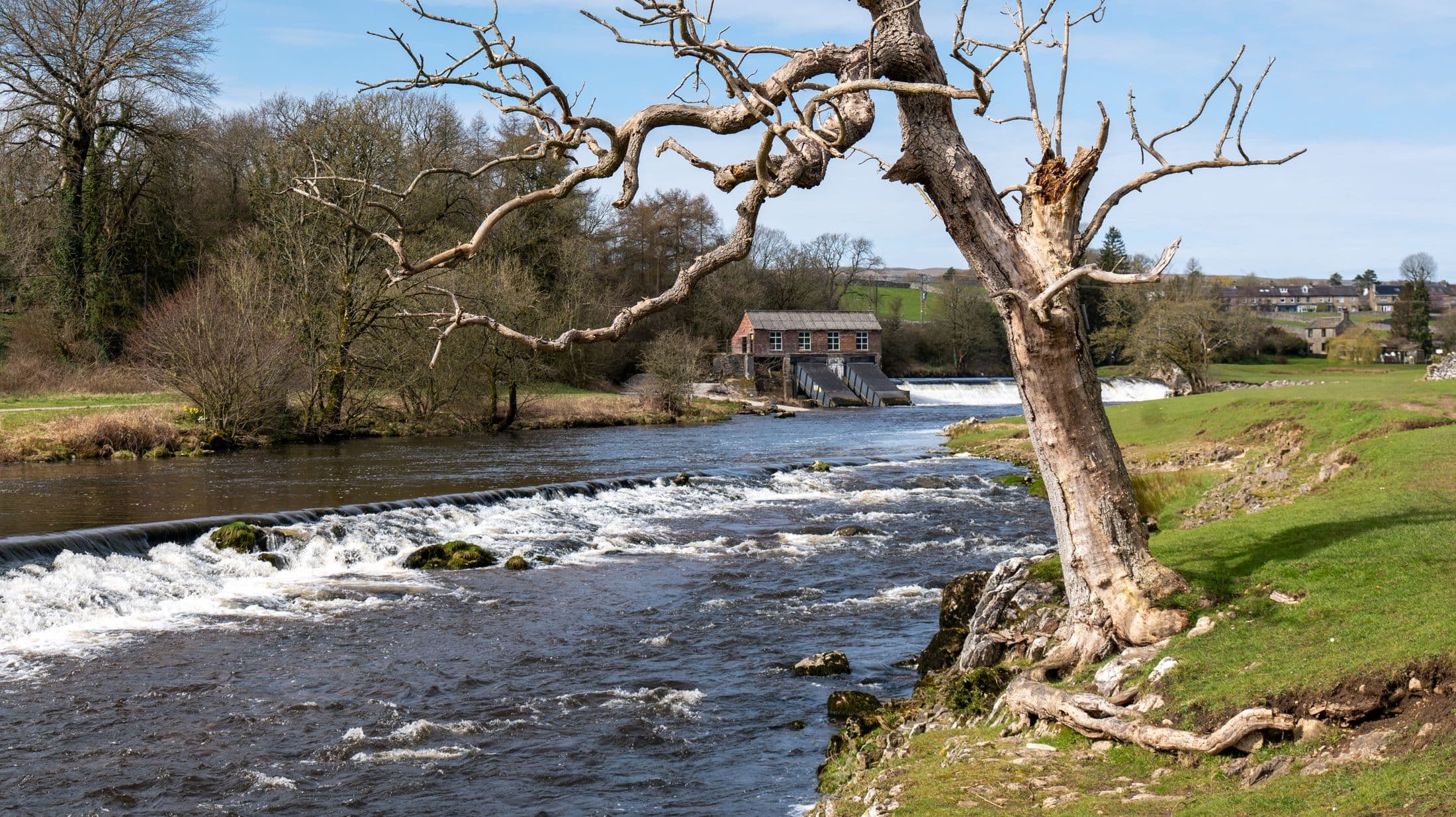 A river stepping over a low weir past an old mill in open countryside