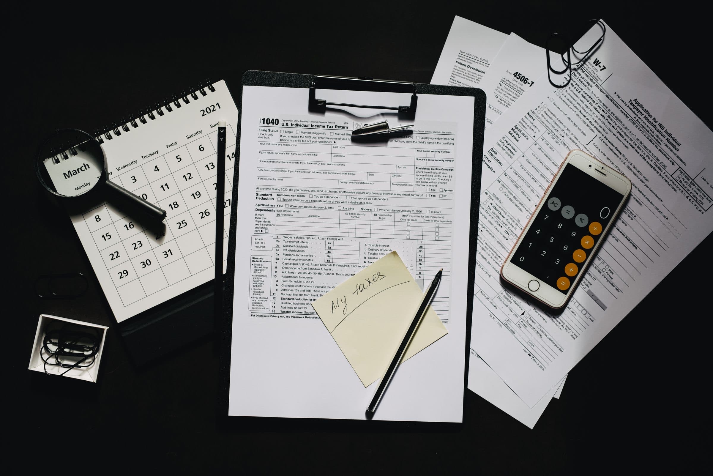 Tax forms, a calculator and a pen on a dark surface, seen from above